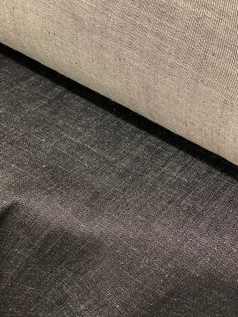 May include: Two pieces of denim fabric, one light gray and one dark gray, are shown side by side. The fabric has a woven texture.