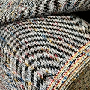 May include: Close-up of a roll of black and white fabric with red, blue, and yellow stripes. The fabric has a textured, speckled appearance.