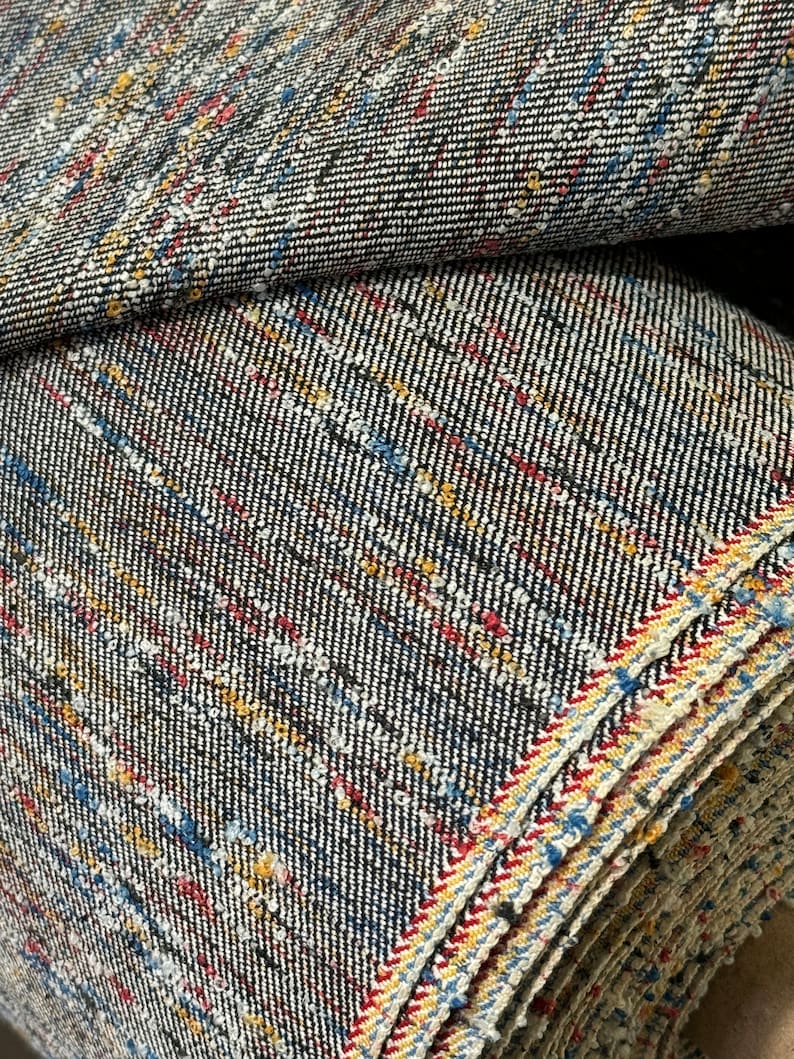 May include: Close-up of a roll of black and white fabric with red, blue, and yellow stripes. The fabric has a textured, speckled appearance.