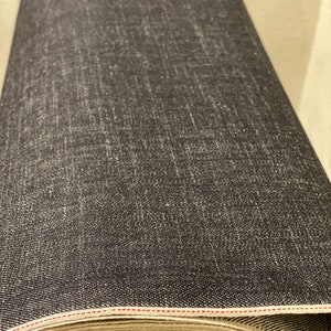May include: A roll of dark blue denim fabric with a red stitching detail. The fabric is rolled up and the end of the roll is visible.