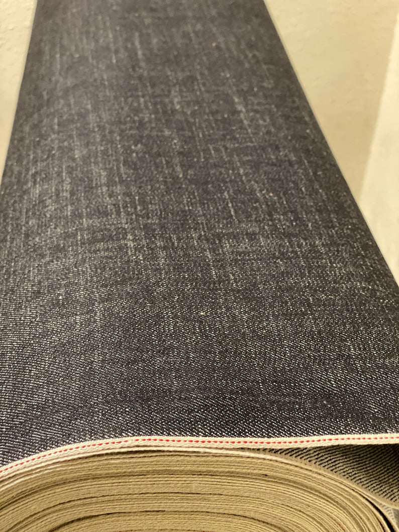 May include: A roll of dark blue denim fabric with a red stitching detail. The fabric is rolled up and the end of the roll is visible.