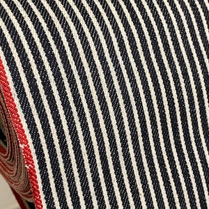May include: Close-up of black and white striped fabric with a red edge. The fabric has a woven texture and is likely used for clothing or home decor.