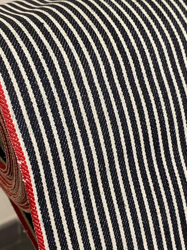 May include: Close-up of black and white striped fabric with a red edge. The fabric has a woven texture and is likely used for clothing or home decor.