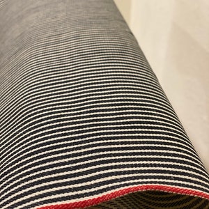 May include: A roll of black and white striped fabric with a red edge. The fabric is woven with a subtle texture.