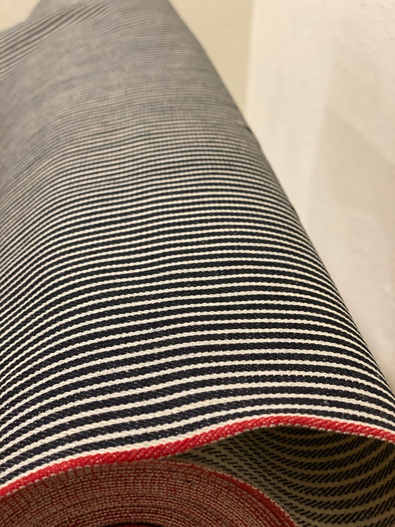 May include: A roll of black and white striped fabric with a red edge. The fabric is woven with a subtle texture.