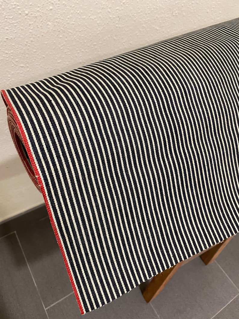 May include: A roll of black and white striped fabric with a red edge. The fabric is woven with a subtle texture.