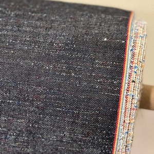 May include: Black denim fabric with a selvedge edge. The edge has a red, yellow, and blue stripe.