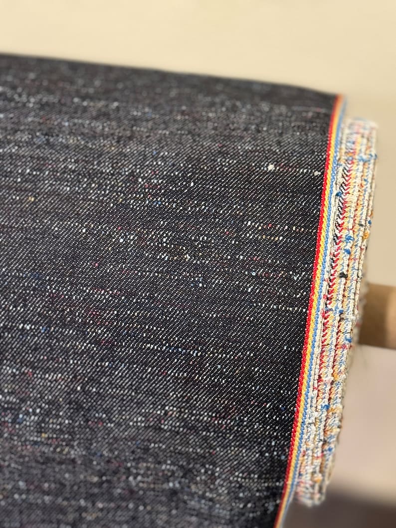 May include: Black denim fabric with a selvedge edge. The edge has a red, yellow, and blue stripe.