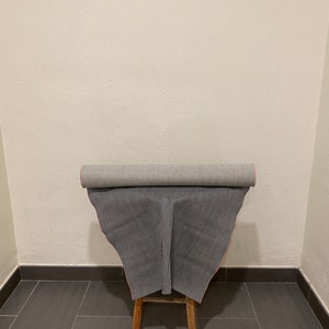 May include: A roll of black and white striped fabric with a red edge is displayed on a wooden stool. The fabric is rolled up and the edges are visible.