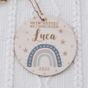 K&ouml;nnte beinhalten: Ein runder Holzanh&auml;nger mit einem Regenbogen, Sternen und dem Text "Mein erstes Weihnachten Luca 2022".