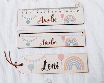 May include: Three wooden rulers with colourful rainbow and balloon designs. The rulers are personalised with the names "Amelie" and "Leni". The top ruler has a measurement scale from 0 to 15.