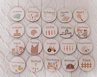 May include: A collection of twenty wooden discs with various illustrations and German words. The discs feature images of a jade roller, makeup, jewelry, games, sports, a stamp, stickers, pencils, a road, superheroes, animals, a dog, a tractor, crayons, watercolors, tools, space, a Viking helmet, and fences.
