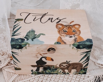 May include: A wooden keepsake box with a light wood finish and a colorful jungle scene. The box has a hinged lid and a metal latch. The box is decorated with a tiger, a toucan, a frog, and a sloth. The box is labeled "Titus".