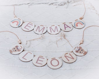 Peut inclure: Deux bannières de nom en bois avec des motifs colorés. La première bannière épelle "EMMA" avec un motif arc-en-ciel à chaque extrémité. La deuxième bannière épelle "LEON" avec un motif d'animal mignon à chaque extrémité.
