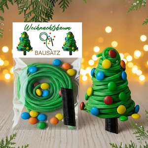 May include: A Christmas tree DIY kit featuring green rubber bands, colourful sweets, and a black base. The kit includes a clear plastic bag with the components and a finished tree model. The packaging has the text "Weihnachtsbaum BAUSATZ".