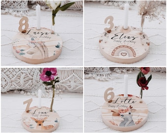 May include: Wooden birthday candle holders with floral and animal designs. Each holder features a number, a name, and the text "Happy Birthday". The holders are decorated with a unicorn, a rainbow, a deer, and a fawn.
