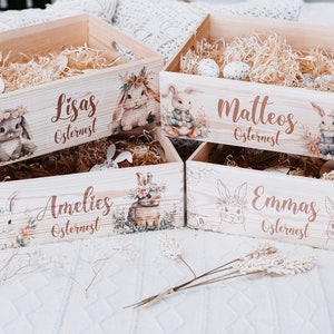 Puede incluir: Cuatro cajas de Pascua de madera con ilustraciones de conejos y nombres: Lisas, Matteos, Amelies y Emmas. Cada caja est&aacute; llena de paja y decorada con detalles florales. Las cajas son de color marr&oacute;n claro.