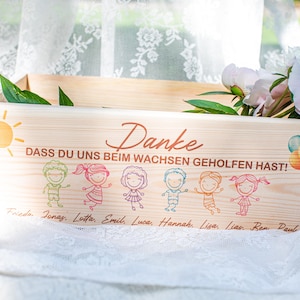 May include: A wooden box with the German word "Danke" and the phrase "DASS DU UNS BEIM WACHSEN GEHOLFEN HAST!" printed on it. The box is decorated with cartoon children, a sun, and balloons. Peonies and greenery are inside the box.