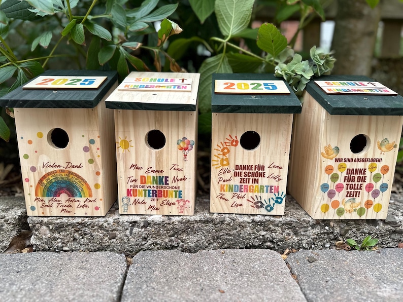 May include: Four wooden birdhouses with dark green roofs, each featuring unique colorful designs and text. One has a rainbow, another has balloons, and two have handprints. The text includes "2025" and "Kindergarten."