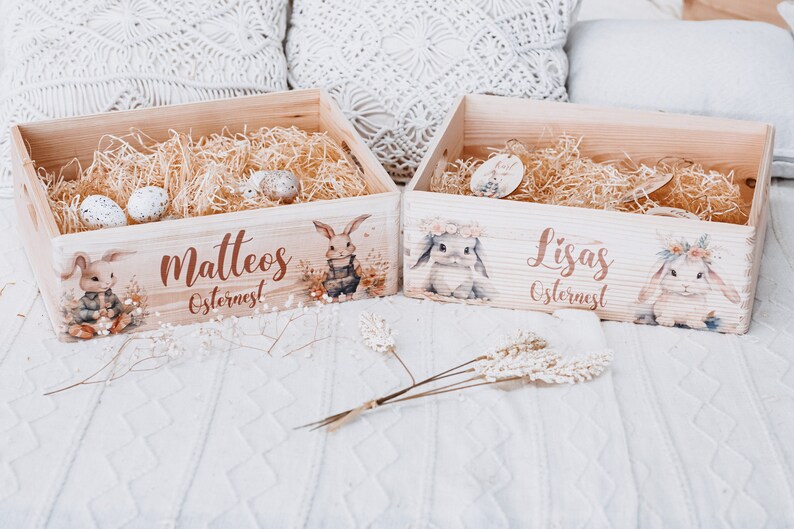 Puede incluir: Dos cajas de Pascua de madera con ilustraciones de conejos y los nombres "Matteos" y "Lisas". Cada caja est&aacute; llena de paja y huevos moteados. Las cajas est&aacute;n decoradas con ilustraciones de conejos en acuarela.