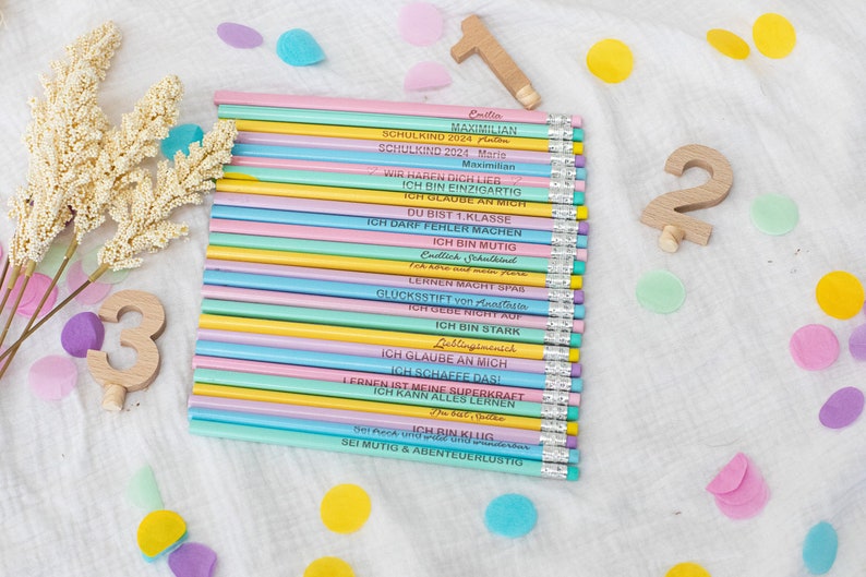 Puede incluir: Un conjunto de 20 l&aacute;pices de colores pastel con mensajes de &aacute;nimo impresos en ellos. Los l&aacute;pices est&aacute;n dispuestos en una pila y est&aacute;n rodeados de confeti de colores.