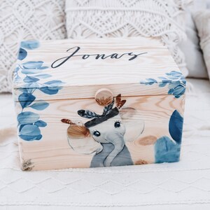 Peut inclure: Une boîte à souvenirs en bois avec un motif floral bleu et blanc et une illustration d'éléphant. La boîte a un couvercle à charnières avec un bouton et est personnalisée avec le nom "Jonas".