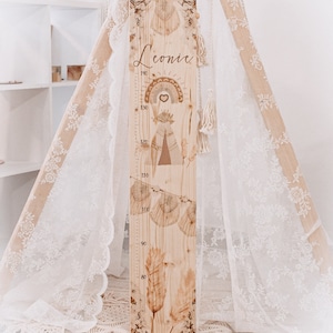 Op de afbeelding: Een houten groeimeter met een boho-ontwerp met een regenboog, hart en tipi. De kaart is gepersonaliseerd met de naam "Leonie" en heeft metingen in centimeters van 60 tot 140.
