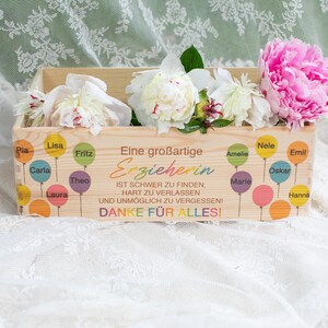 May include: A wooden box filled with white and pink peonies. The box is decorated with colorful balloons and text in German that reads "Eine gro&szlig;artige Erzieherin" (A great educator) and "DANKE F&Uuml;R ALLES!" (THANK YOU FOR EVERYTHING!).