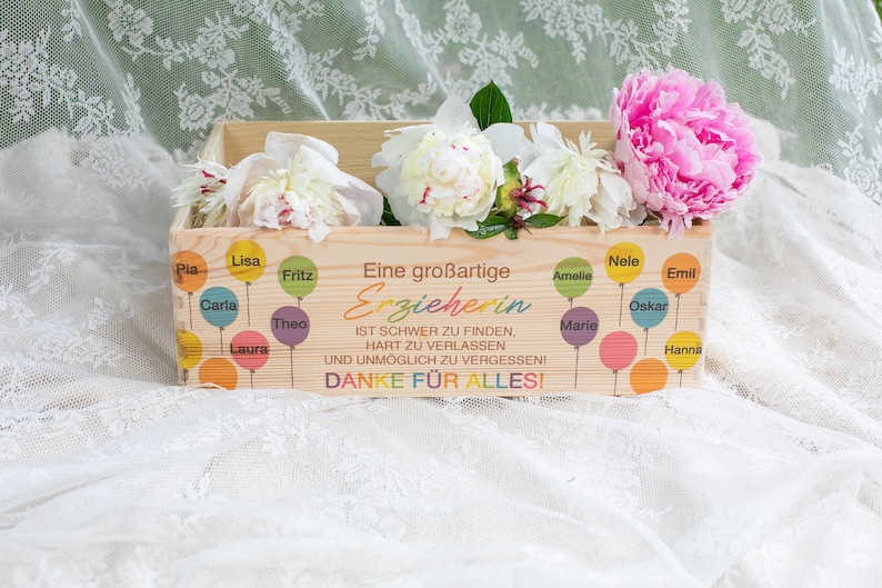 May include: A wooden box filled with white and pink peonies. The box is decorated with colorful balloons and text in German that reads "Eine gro&szlig;artige Erzieherin" (A great educator) and "DANKE F&Uuml;R ALLES!" (THANK YOU FOR EVERYTHING!).