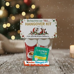 Puede incluir: Una bolsa de plástico transparente que contiene un kit para la resaca. El kit incluye dos tazas de espresso rojas, un paquete verde de Aspirina Plus y una barra de chocolate Kinder Riegel. Una tarjeta en la parte superior dice "HANGOVER KIT".