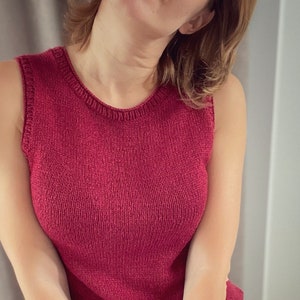 Puede incluir: Un top de punto rojo sin mangas con cuello redondo. El top se lleva sobre una falda blanca con un estampado abstracto de colores.