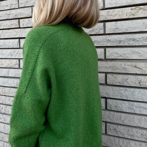May include: A green knitted sweater with long sleeves. The sweater is made of a soft, comfortable material.