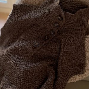 May include: A brown knitted sweater with a high neck and a row of buttons down the front.