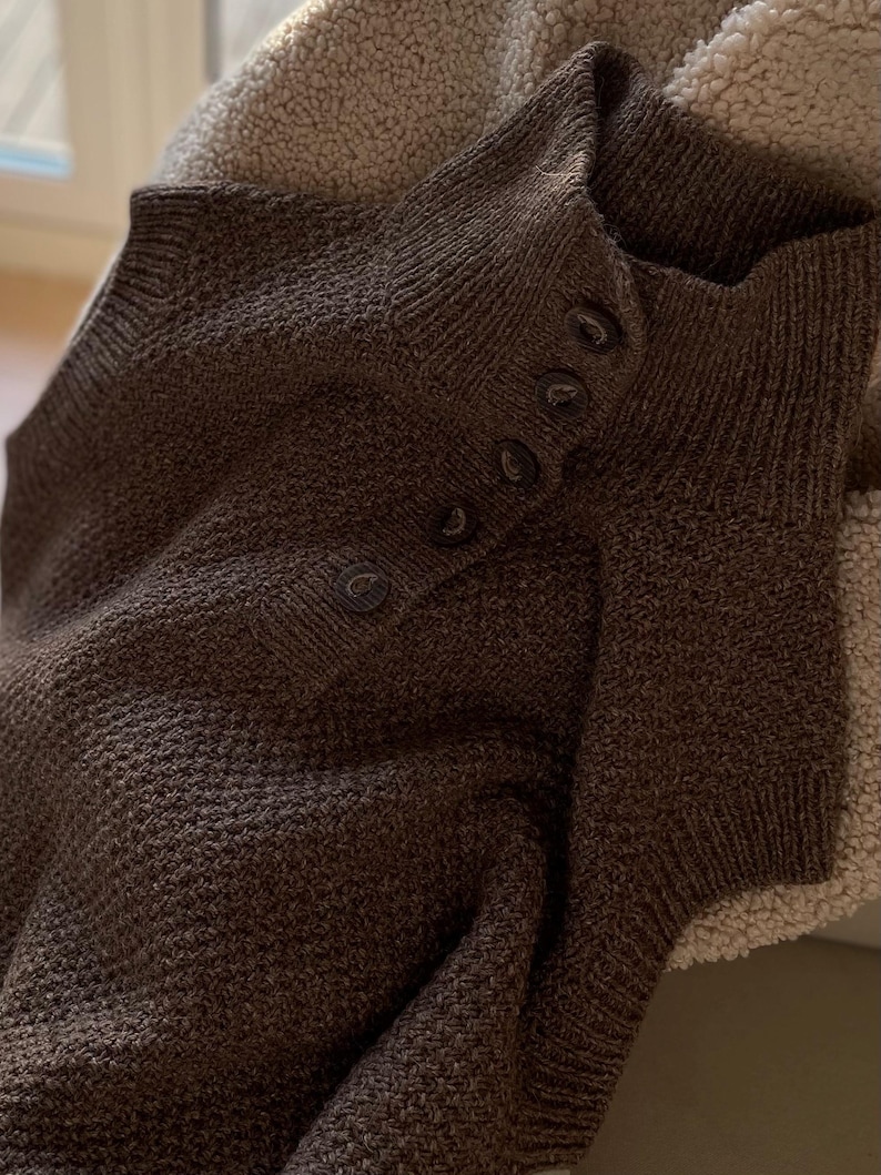 May include: A brown knitted sweater with a high neck and a row of buttons down the front.