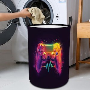 May include: A black laundry hamper with a colorful video game controller design. The controller is a rainbow of colors with a heartbeat graphic below it.