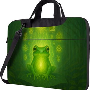 May include: Green laptop bag with a frog illustration. The frog is depicted with a soft glow and surrounded by symbols. The bag has a black handle and a detachable shoulder strap. The bag is designed to carry a laptop.