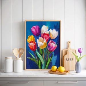 May include: A framed painting of colorful tulips in shades of pink, yellow, red, and white against a deep blue background. The artwork is displayed on a white countertop with kitchen accessories.