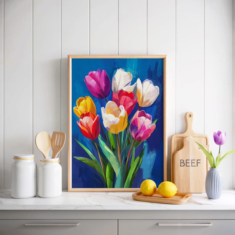 May include: A framed painting of colorful tulips in shades of pink, yellow, red, and white against a deep blue background. The artwork is displayed on a white countertop with kitchen accessories.