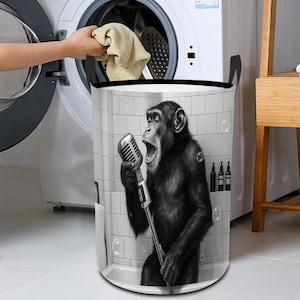 May include: A black and white laundry hamper featuring a chimpanzee singing into a vintage microphone. The hamper has a rectangular shape with a black rim and handles. The background shows a tiled wall and bubbles.