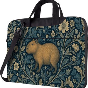 Op de afbeelding: Laptoptas met een capibara-illustratie. De tas heeft een zwart handvat en schouderriem. Het ontwerp bevat een donkerblauw bloemenpatroon met beige en lichtblauwe accenten. De capibara is lichtbruin van kleur.