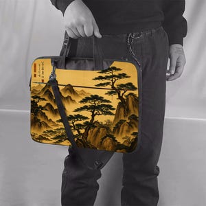 May include: A laptop bag featuring an Asian landscape painting with mountains, trees, and a golden sky. The bag has a black shoulder strap and handle. The artwork is in shades of brown, gold, and green.