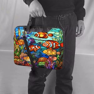 Può includere: Borsa per laptop colorata con un design a vetrata raffigurante pesci pagliaccio che nuotano tra coralli e alghe. La borsa ha un manico nero e una tracolla nera. Lo sfondo è un vivace mix di blu, verdi e arancioni.