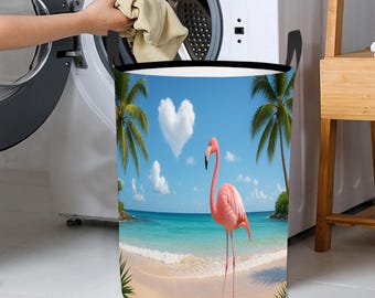 May include: A round laundry basket with a tropical beach scene featuring a pink flamingo, palm trees, and a heart-shaped cloud. The basket has black handles and a black rim. A person is putting clothes into a washing machine.
