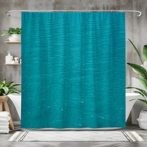 May include: A teal shower curtain with a rippled water design. The curtain hangs from a silver rod and is made of a soft, flowing material. The design resembles the surface of a body of water.