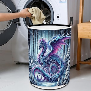 Puede incluir: Un cesto de ropa blanco con un cordón de ajuste negro y una imagen colorida de un dragón morado y azul en un bosque nevado.
