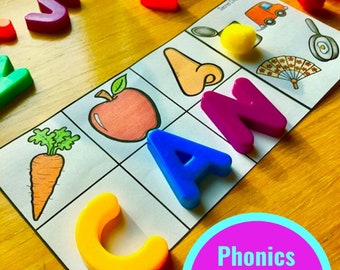 May include: A colourful alphabet learning game for children. The game features a grid with pictures of a carrot, apple, nose, and a fan.  The letters C, A, and N are placed on the grid.  The letters are colourful and made of plastic.  The game is labelled "Phonics Kindergarten CVC".