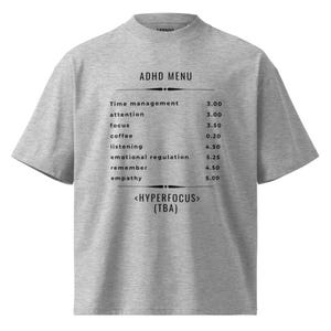 May include: A grey t-shirt with a high neck. The shirt displays the text "ADHD MENU" above a list of items with prices, such as "Time management," "attention," and "focus." Below the list is "<HYPERFOCUS> (TBA)."