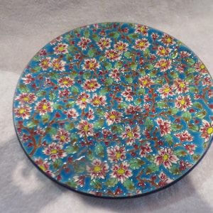 Pode incluir: Um prato de cerâmica azul com um design floral. O prato é decorado com flores brancas, cor-de-rosa e amarelas sobre um fundo azul.