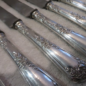 May include: A set of six silver dinner knives with ornate, floral-patterned handles.