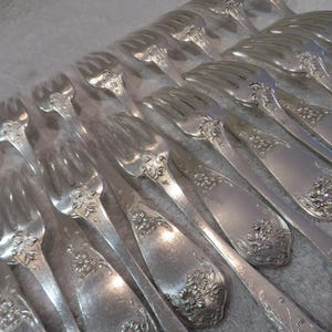 Può includere: Un set di forchette d'argento con decorazioni floreali ornate. Le forchette sono disposte in fila, con i manici rivolti a destra. Le forchette sono tutte a fuoco, e lo sfondo è sfocato.